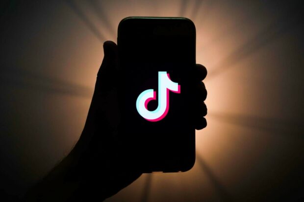A hand holding a phone with a TikTok logo glowing on the screen in dark lighting