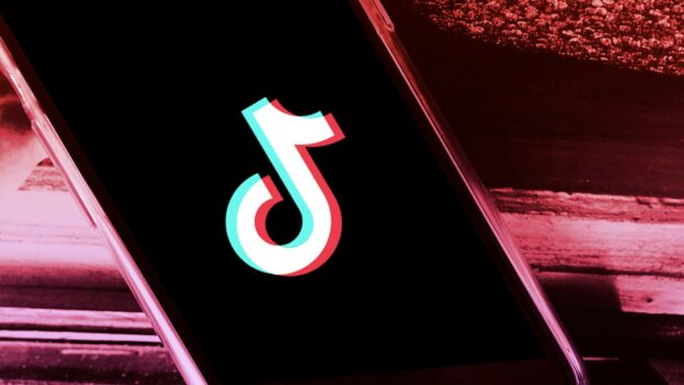 A close up shot of TikTok logo displayed on a phone screen in a dimly lit setting
