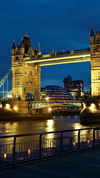 The River Thames flows beneath the illuminated Tower Bridge with city buildings in the background