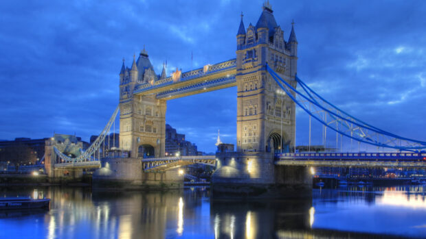 Tower Bridge over the River Thames is beautifully illuminated during dusk with reflections on the water, 4K Wallpaper