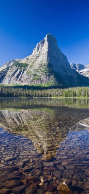 A towering mountain peak reflects in a clear lake at Glacier National Park, HD Phone Wallpaper