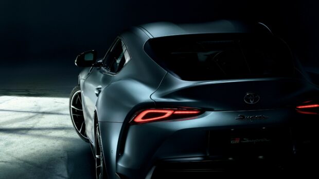 Luxury silver Toyota Supra sports car in a dark, moody setting with sleek design and LED taillights.