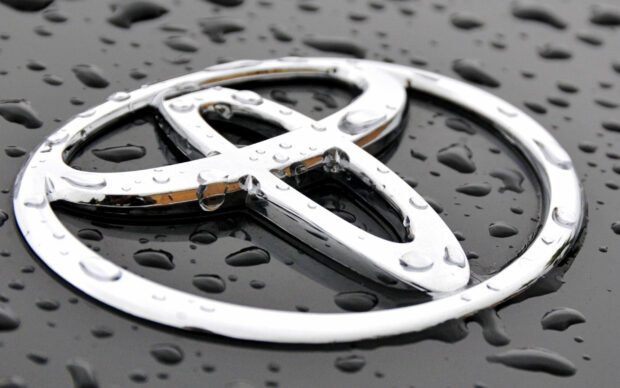 Shiny silver car emblem on wet black surface with water droplets.