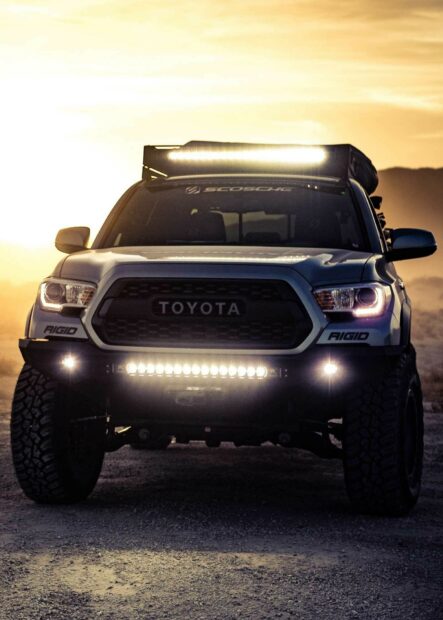 Off-road Toyota truck with LED light bar and rugged tires during sunset.