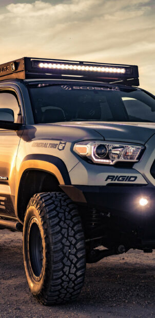 Off-road vehicle with LED light bar, rugged tires, and custom decals in a desert setting during sunset.