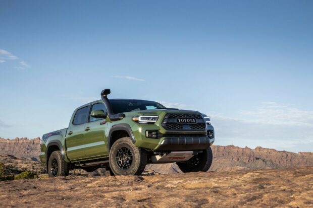 Off-road green Toyota Tacoma pickup truck in rugged desert scenery with mountains in the background, showcasing durability and outdoor adventure-ready design.