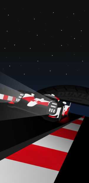 Race car at night on race track with tire in background.