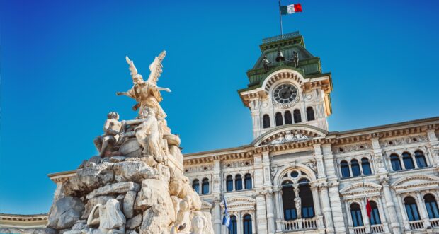 Trieste features historic architecture with statues and a clock tower under a clear blue sky, 2K Desktop Wallpaper