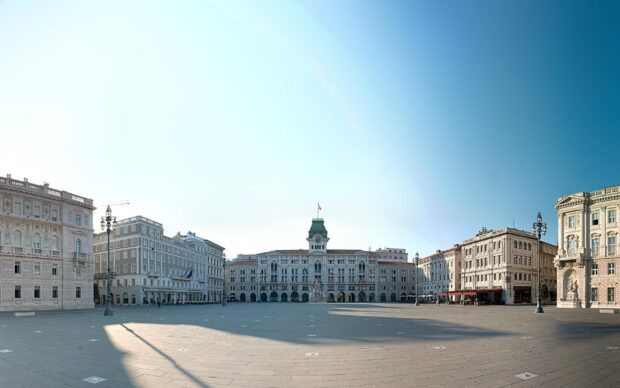A wide view of Trieste city square surrounded by historic buildings under clear blue sky, 2K Desktop Wallpaper