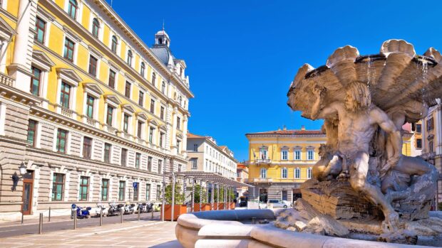 A detailed statue fountain stands in a vibrant Trieste city square with classic buildings, 2K Desktop Wallpaper