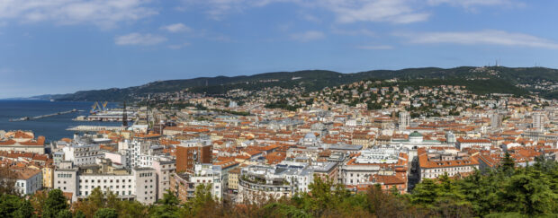 A panoramic view of Trieste shows its cityscape and coastline under a clear sky, 2K Desktop Wallpaper