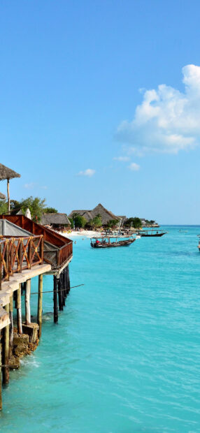 A tropical Zanzibar scene shows boats floating near wooden piers under blue sky, HD Mobile Wallpaper