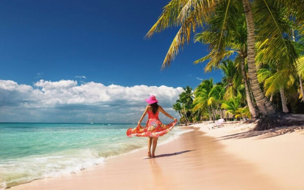 A woman in a pink hat walking along a tropical beach in the Dominican Republic, 2K Desktop Wallpaper
