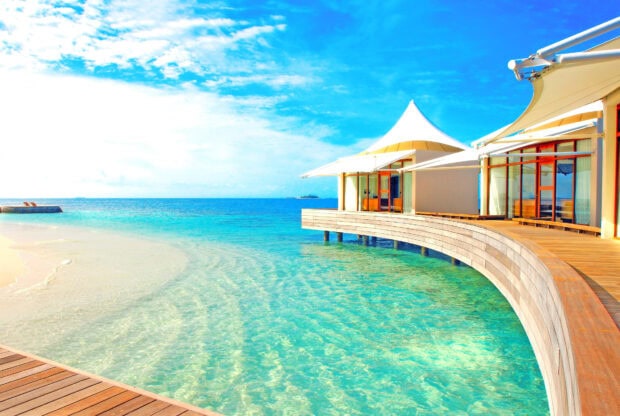 A tropical bungalow stands over clear blue ocean water with a bright sky, HD Desktop Wallpaper
