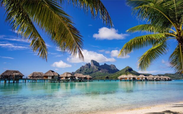 A clear view of bungalow villas over tropical turquoise water with mountains, 2K Desktop Wallpaper