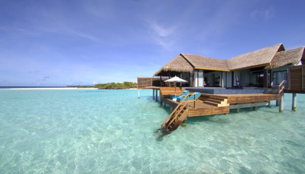A tropical bungalow overlooks clear blue ocean waters under a bright sky in this bungalow wallpapers, Desktop Wallpaper