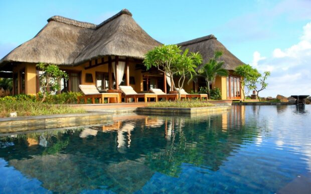 A tropical bungalow with thatched roof reflects beautifully in the calm pool water, 2K Desktop Wallpaper