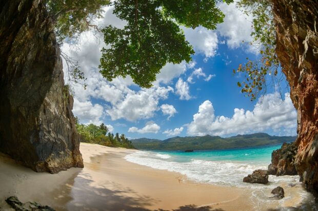 A sandy Dominican Republic beach with turquoise water and rocky cliffs under a blue sky, HD Desktop Wallpaper