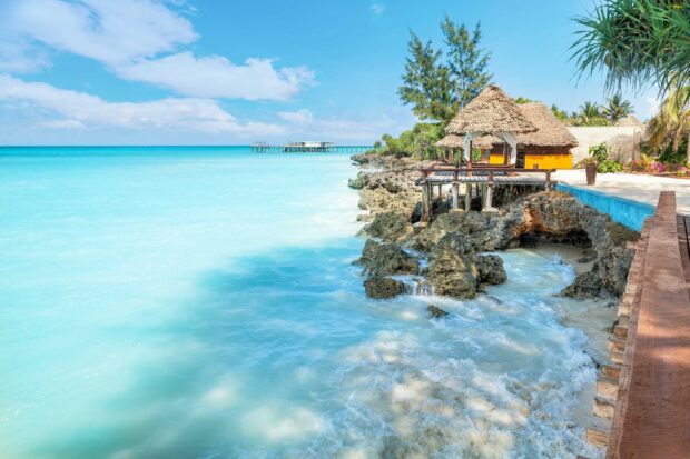 A scenic coastline in Zanzibar with clear blue water and beach huts, HD Desktop Wallpaper