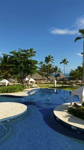 A tropical resort in the Dominican Republic features a large pool surrounded by palm trees and cabanas, 4K Mobile Wallpaper