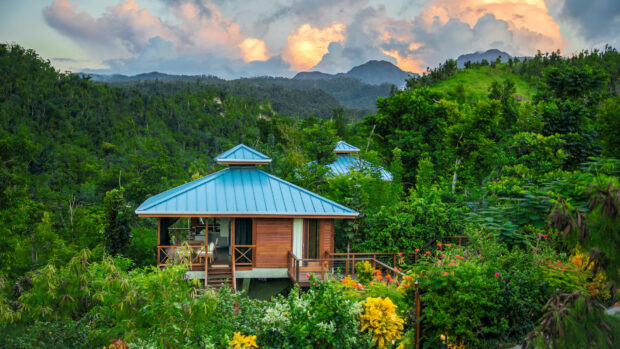 A wooden house surrounded by lush greenery on Dominica Island is captured at sunset, HD Desktop Wallpaper
