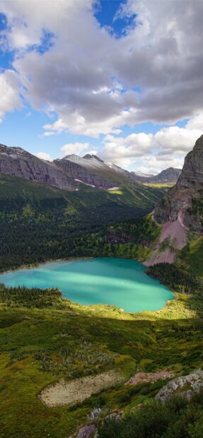 A turquoise lake surrounded by mountains in Glacier National Park under a cloudy sky, 2K Mobile Wallpaper