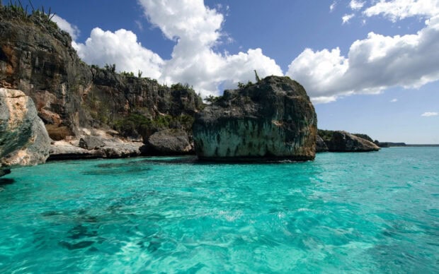 Clear turquoise water surrounds rugged cliffs under a bright blue sky with clouds in the Dominican Republic, 2K Desktop Wallpaper