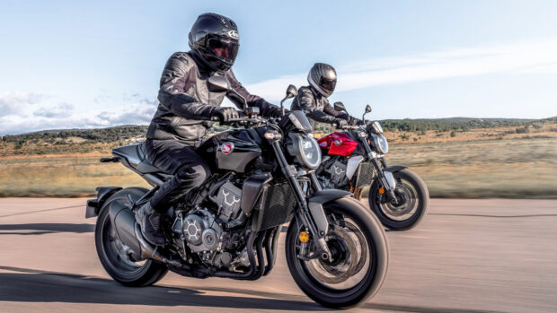 High-performance black and red motorcycles being ridden on open road by motorcyclists wearing full gear under blue sky.