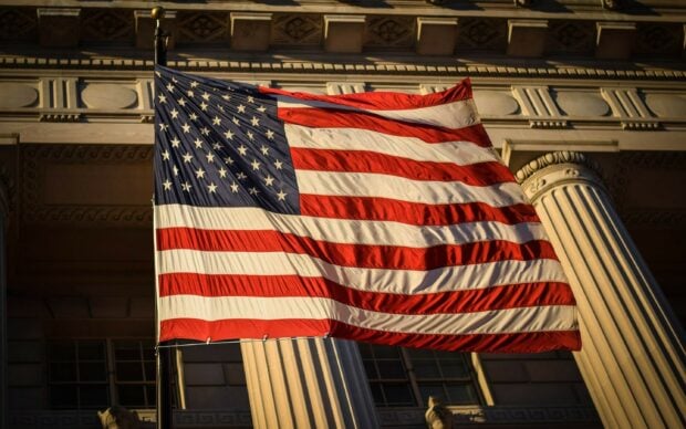 American flag waving in front of a historic building with architectural columns and windows