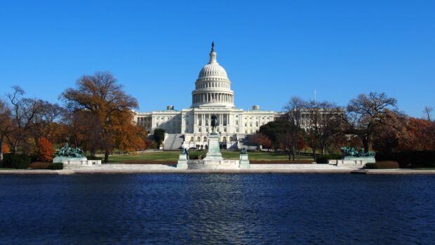 The United States Capitol building surrounded by autumn trees and reflected in a water body