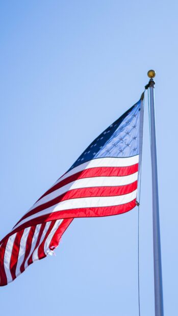 United States flag waving on the flagpole against clear blue sky
