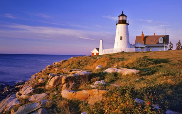 A scenic United States lighthouse on a rocky coastline at sunset