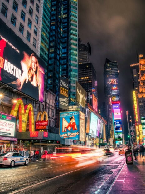 Busy street in New York City with bright billboards and McDonald's sign at night