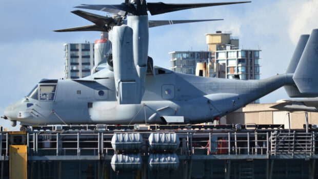A detailed view of V 22 Osprey aircraft parked on a naval ship with city buildings in the background