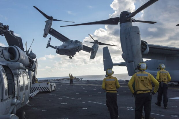 Crew members guide the V 22 Osprey aircraft landing on the aircraft carrier deck