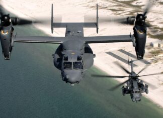 Military V 22 Osprey flying over coastal water near sandy shore