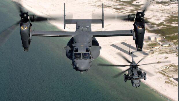 Military V 22 Osprey flying over coastal water near sandy shore