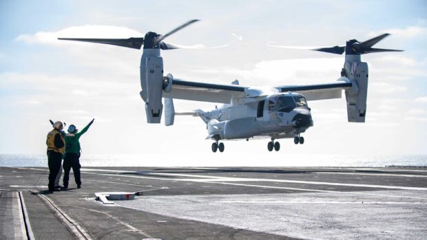 Two crew members guiding a V 22 Osprey aircraft landing on a naval ship deck