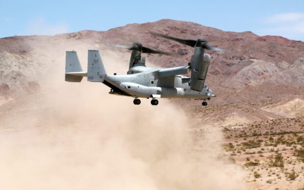 V 22 Osprey aircraft flying over desert terrain with mountains in the background