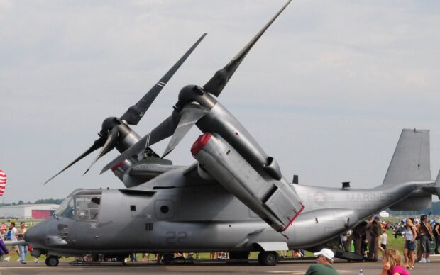 A gray V 22 Osprey aircraft parked on a runway with people around it
