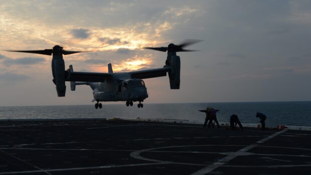 V 22 Osprey aircraft landing on a ship deck during sunset with crew members signaling
