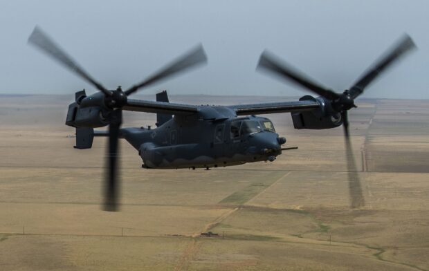 Military V 22 Osprey flying over open terrain in daylight