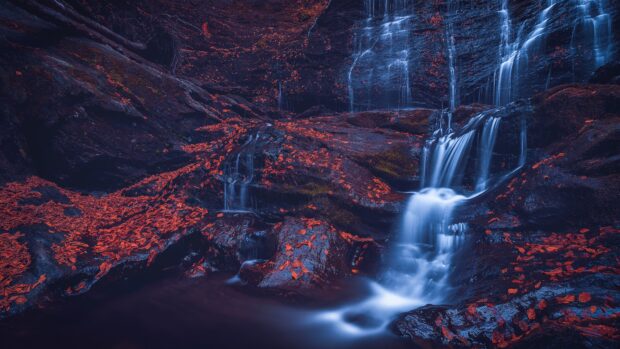 A serene waterfall flows over rocks surrounded by bright red leaves in Vermont, 4K PC Wallpaper