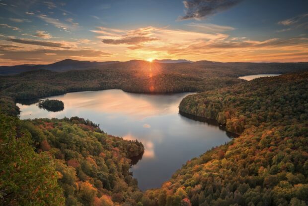 The Vermont Wallpapers showcase a beautiful lake surrounded by autumn forests with the sun setting behind mountains, HD Desktop Wallpaper