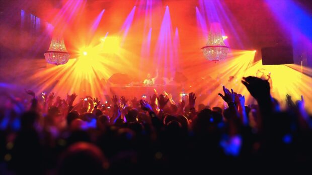 A vibrant nightclub scene shows a DJ performing with colorful lights and a lively crowd, HD Desktop Wallpaper