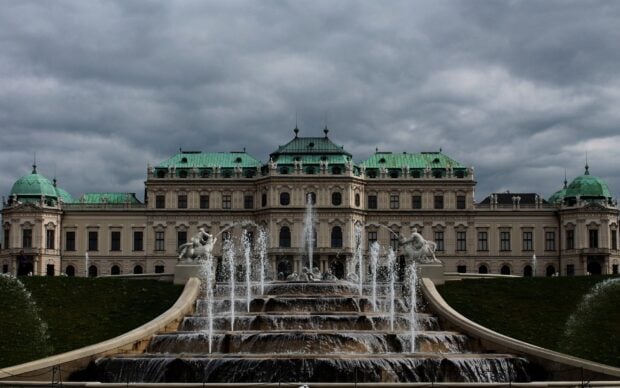 Historic Vienna palace with green rooftops and fountain under cloudy sky