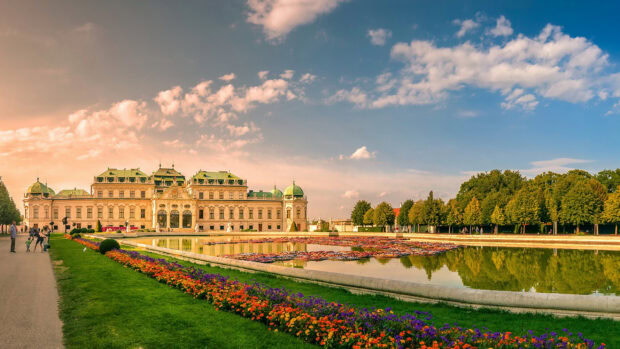 The Belvedere Palace in Vienna Austria with colorful flowers and a reflective pond under a cloudy sky
