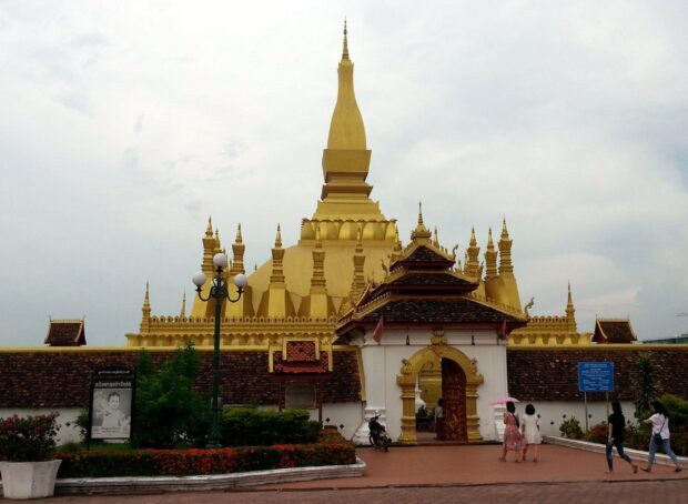 The golden stupa of a historic temple in Vientiane with visitors walking nearby