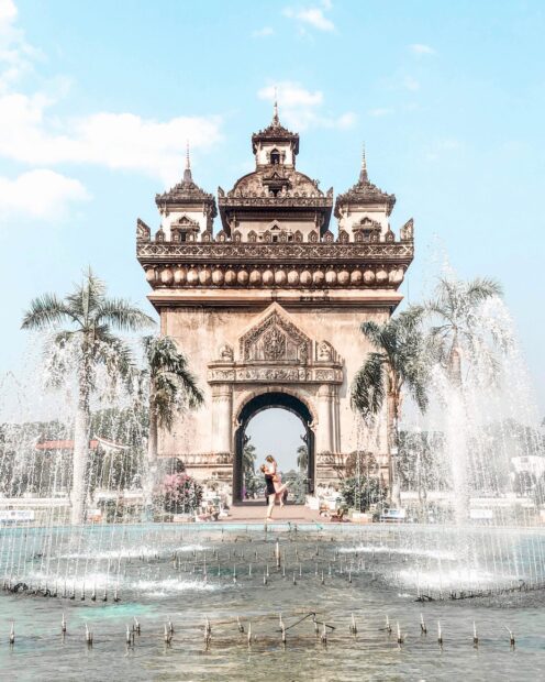The Patuxai monument in Vientiane with water fountains and palm trees under a clear blue sky