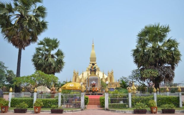 The Vientiane statue surrounded by palm trees in front of golden stupa